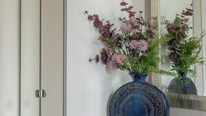 Une chambre moderne avec une armoire blanche, un vase bleu rempli de fleurs, un livre posé sur une table et un miroir qui reflète la pièce.