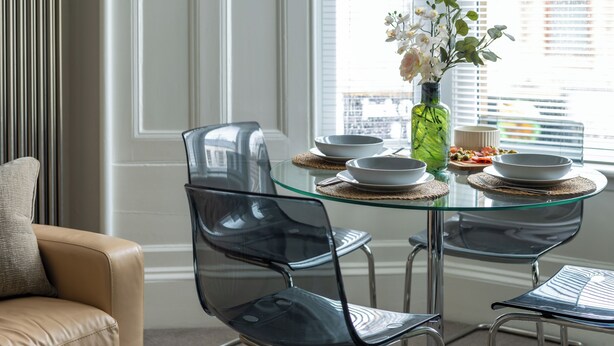 Un coin repas avec une table en verre, des chaises transparentes et un vase rempli de fleurs.