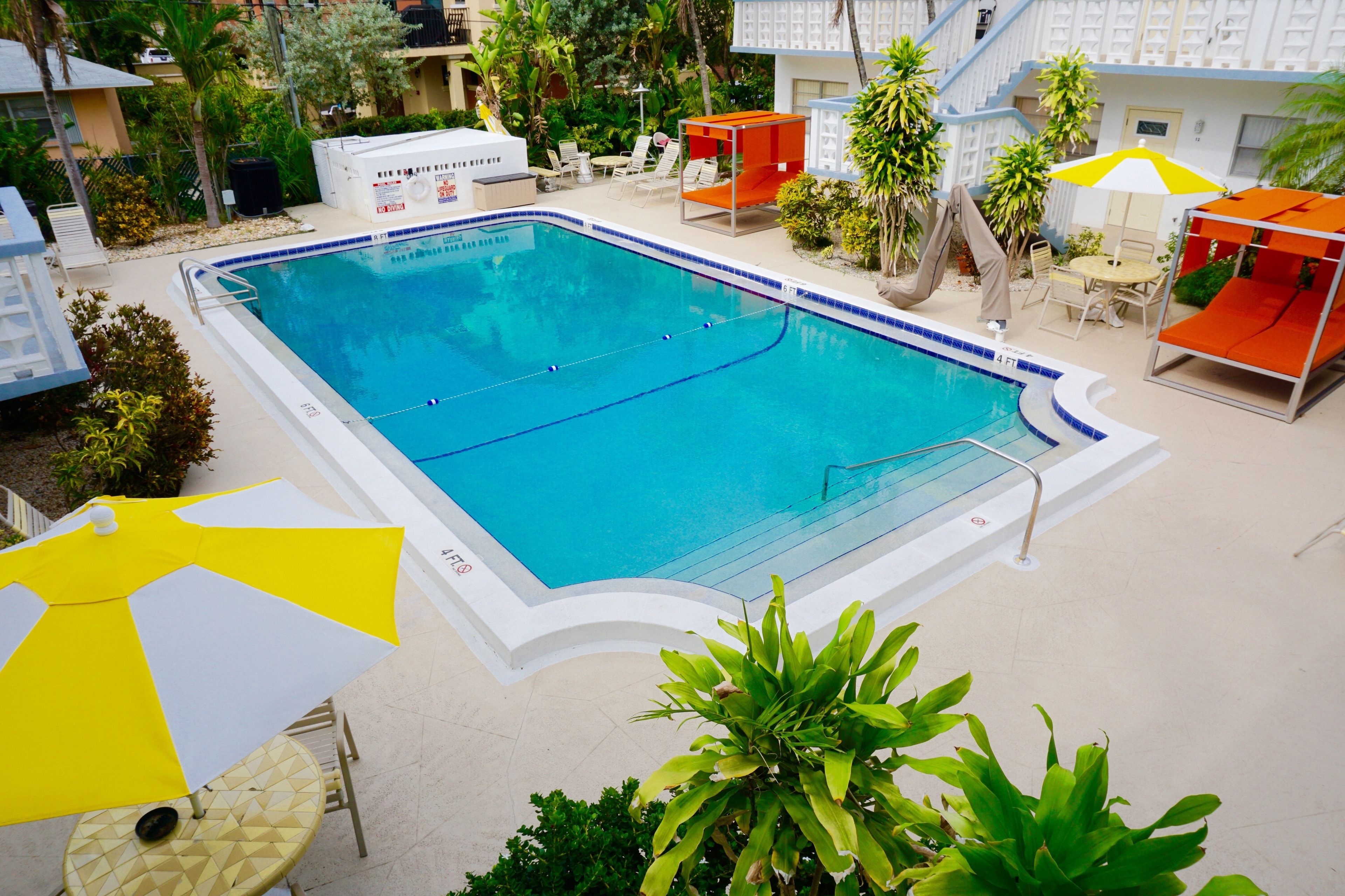 A rectangular swimming pool with a white and blue tiled edge, surrounded by outdoor seating and umbrellas.