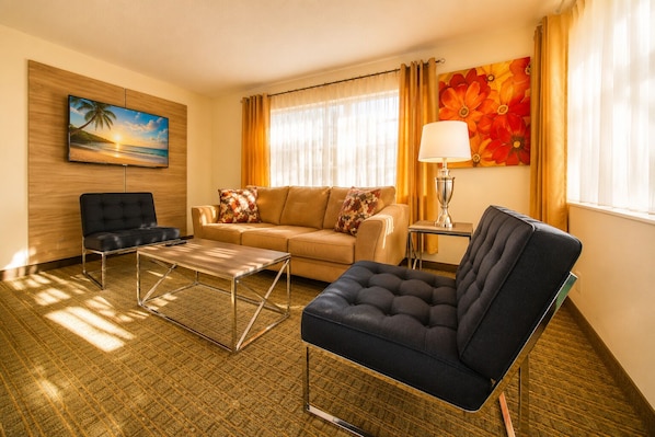A hotel room with a sofa, armchair, coffee table, and a painting on the wall. - Club Lux Resort By the Beach (Deerfield Beach)