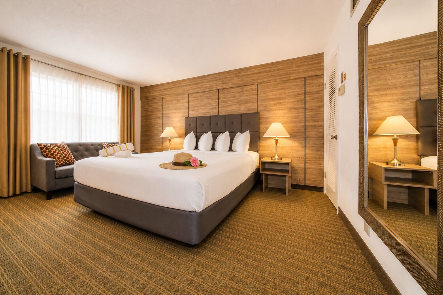 A hotel room with a large bed, two bedside tables, a sofa, a mirror, and a window with curtains.
