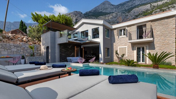 Ein modernes Haus mit Pool, Steinmauern und einer Bergkulisse.