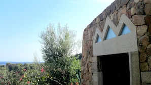 Edificio de piedra con un diseño de ventana triangular, rodeado de follaje y un cielo despejado.