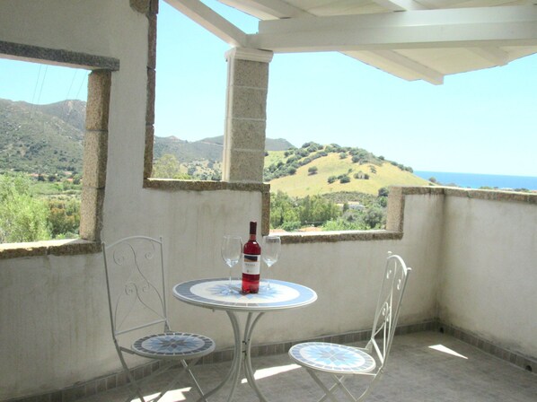 A balcony with a table and chairs, a bottle of wine, and a view of a hilly landscape.