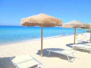 A beach with thatched umbrellas and sun loungers.