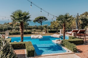 A pool area with a view of the sea, surrounded by palm trees and lounge chairs. - Talici Hill - Rustic Villas (Sutomore)