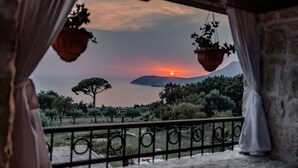 Un balcon offrant une vue sur un coucher de soleil au-dessus d’une étendue d’eau et d’une montagne.