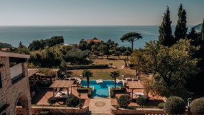 A pool area with a view of the sea, surrounded by trees and a stone building. - Talici Hill - Rustic Villas (Sutomore)