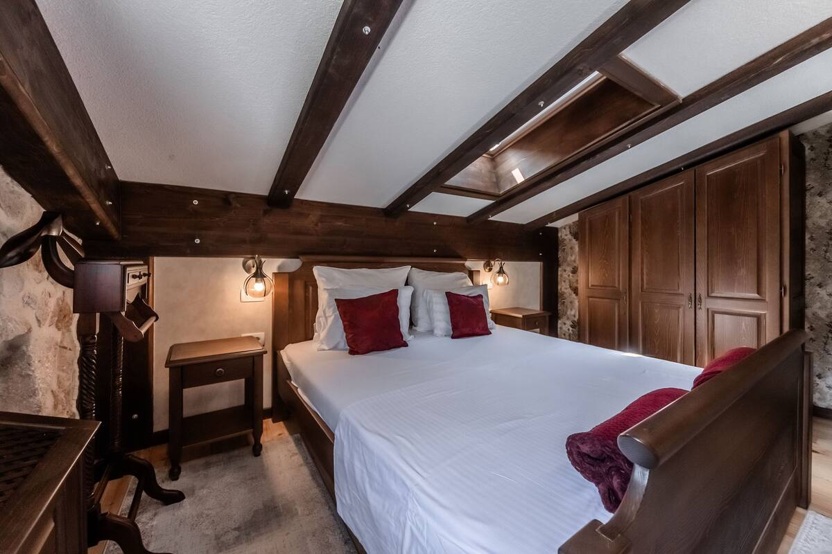 A bedroom with a wooden ceiling, a large bed with white and red bedding, a nightstand, and a wardrobe.
