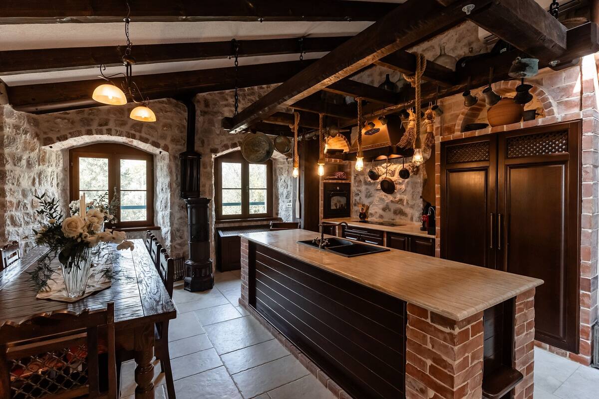 A rustic kitchen with exposed brick walls, wooden beams, and hanging pots.