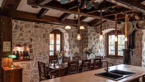 Une cuisine rustique aux murs de pierre, avec des poutres en bois, des ustensiles de cuisine suspendus et un grand îlot central doté d’un évier.