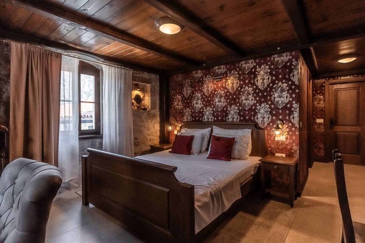 A bedroom with a wooden bed, a nightstand, a chair, and a window with curtains.