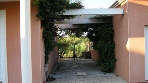 A covered walkway with a column and a door on the left, leading to a building with a pink facade. - Independent villa with pool (Agde)