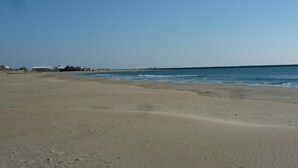 A wide sandy beach with a calm sea, a clear sky, and distant buildings. - Independent villa with pool (Agde)