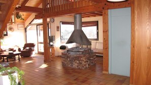 Un salon chaleureux avec une cheminée en pierre, des poutres apparentes en bois au plafond et une grande fenêtre.