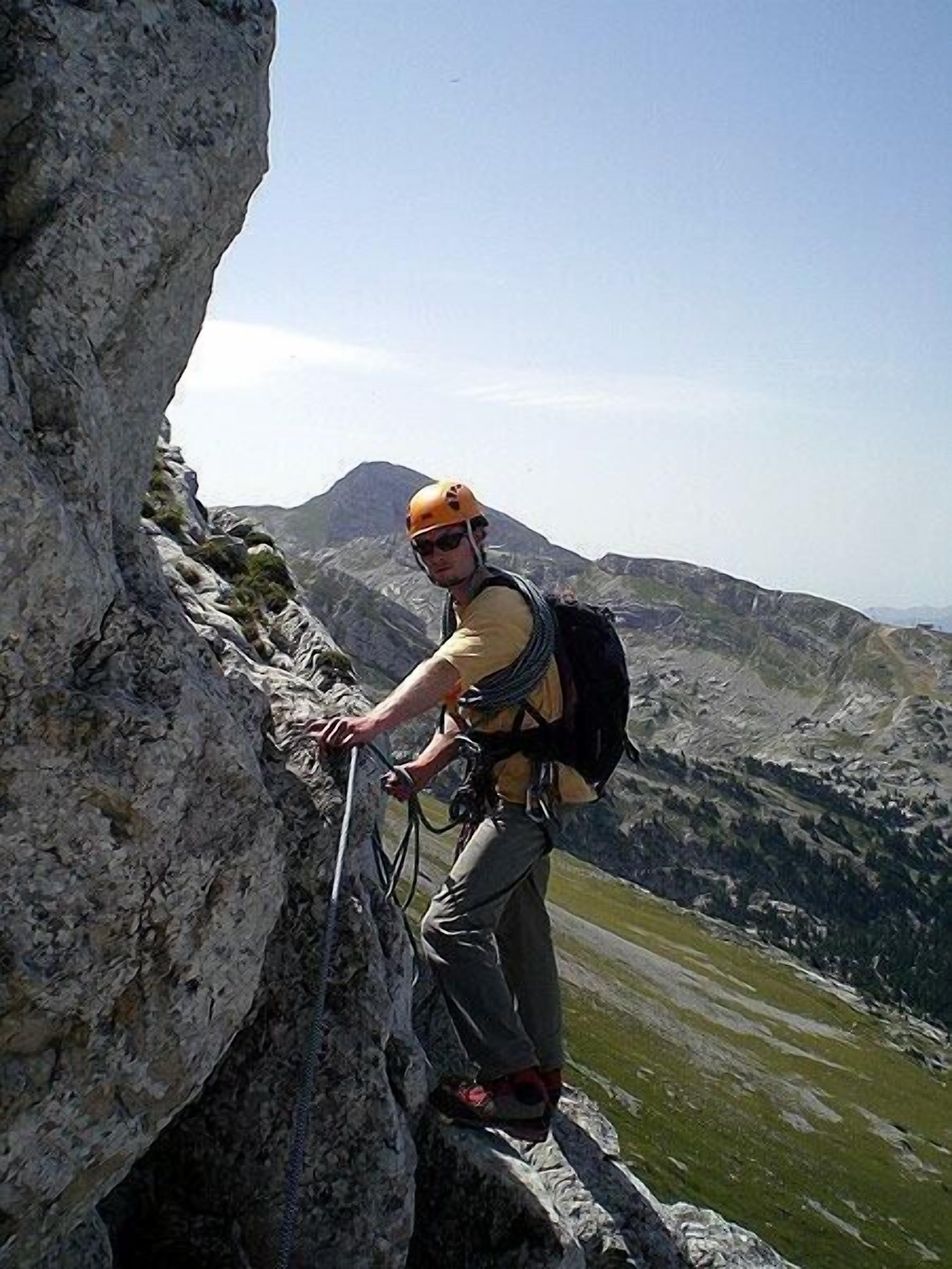 Eine Person besteigt einen steinigen Bergpfad mit Rucksack, umgeben von einer gebirgigen Landschaft.