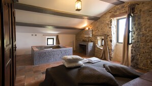 A rustic room with a stone wall, a fireplace, a bathtub, and a bed with pillows. - Independent Mas not overlooked with 10700m2 of enclosed park, 14x4 heated pool  (Labeaume)