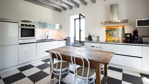 A modern kitchen with white cabinetry, a wooden dining table, and checkered flooring. - Independent Mas not overlooked with 10700m2 of enclosed park, 14x4 heated pool  (Labeaume)