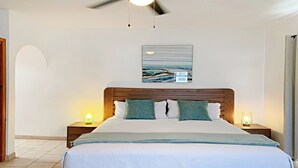 Ein Schlafzimmer mit einem hölzernen Kopfteil, einem großen Bett mit weißer Bettwäsche, zwei Nachttischlampen und einem Deckenventilator.