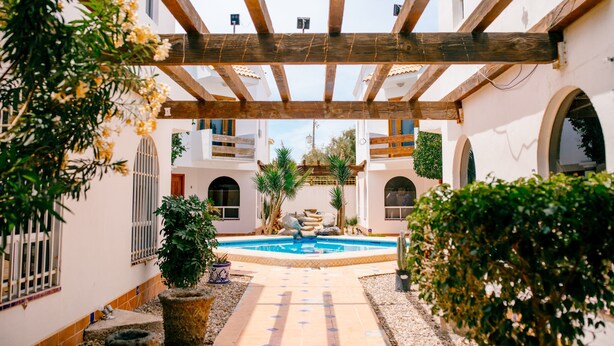 Ein Innenhof mit Pool, einer Holz-Pergola und Blumentöpfen.