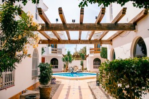 Un patio con una pérgola de madera, una piscina y plantas en macetas.