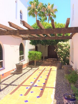 Un patio con piso de baldosas, una pérgola, plantas en macetas y una palmera.