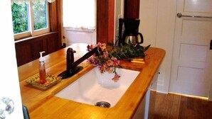 A kitchen with a wooden countertop, a sink, a coffee maker, and a window with curtains. - Sweet, Historic Cottage on Carmel Point (Carmel)