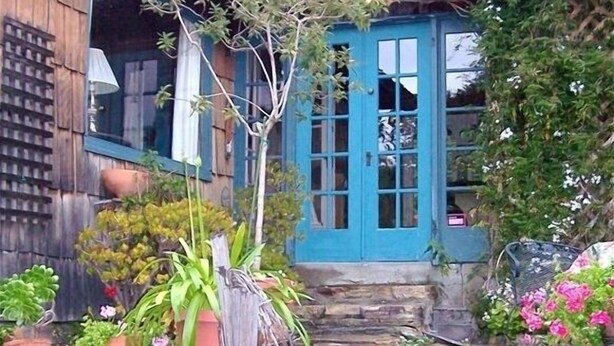A rustic wooden house with a blue door, stone steps, and various potted plants. - Sweet, Historic Cottage on Carmel Point (Carmel)