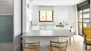 A modern kitchen with white cabinets, a glass dining table, and a window with curtains. - MAMAD Cosy Hideaway steps from Beach by FeelHome (Tel Aviv - Jaffa)