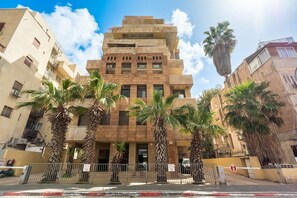 Un edificio de varios pisos con una entrada central, rodeado de palmeras y un acceso con puerta cerrada y un letrero de 'No Entrar'.