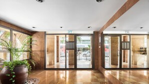 A hotel lobby with a checkered floor, large potted plants, and glass doors leading outside. - MAMAD Cosy Hideaway steps from Beach by FeelHome (Tel Aviv - Jaffa)