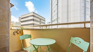 A balcony with a green metal table and chairs, a wall-mounted light fixture, and a view of a building in the background. - MAMAD Cosy Hideaway steps from Beach by FeelHome (Tel Aviv - Jaffa)