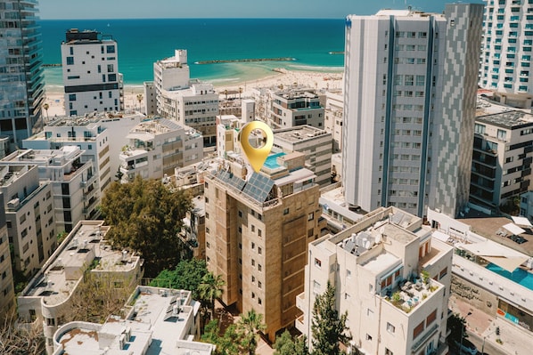 Un immeuble de grande hauteur doté d’une piscine sur le toit, entouré d’autres bâtiments et avec une plage en arrière-plan.