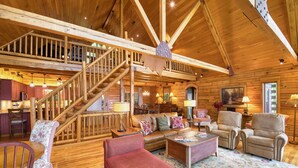 A spacious log cabin interior with a wooden staircase, a cozy living area with a fireplace, and a dining area with wooden cabinets. - 4 BR Mountain cabin with beautiful long range views in quiet gated community (Maggie Valley)