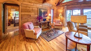 A cozy cabin interior with wooden walls, a fireplace, a dining area, and large windows offering a view of the outdoors. - 4 BR Mountain cabin with beautiful long range views in quiet gated community (Maggie Valley)