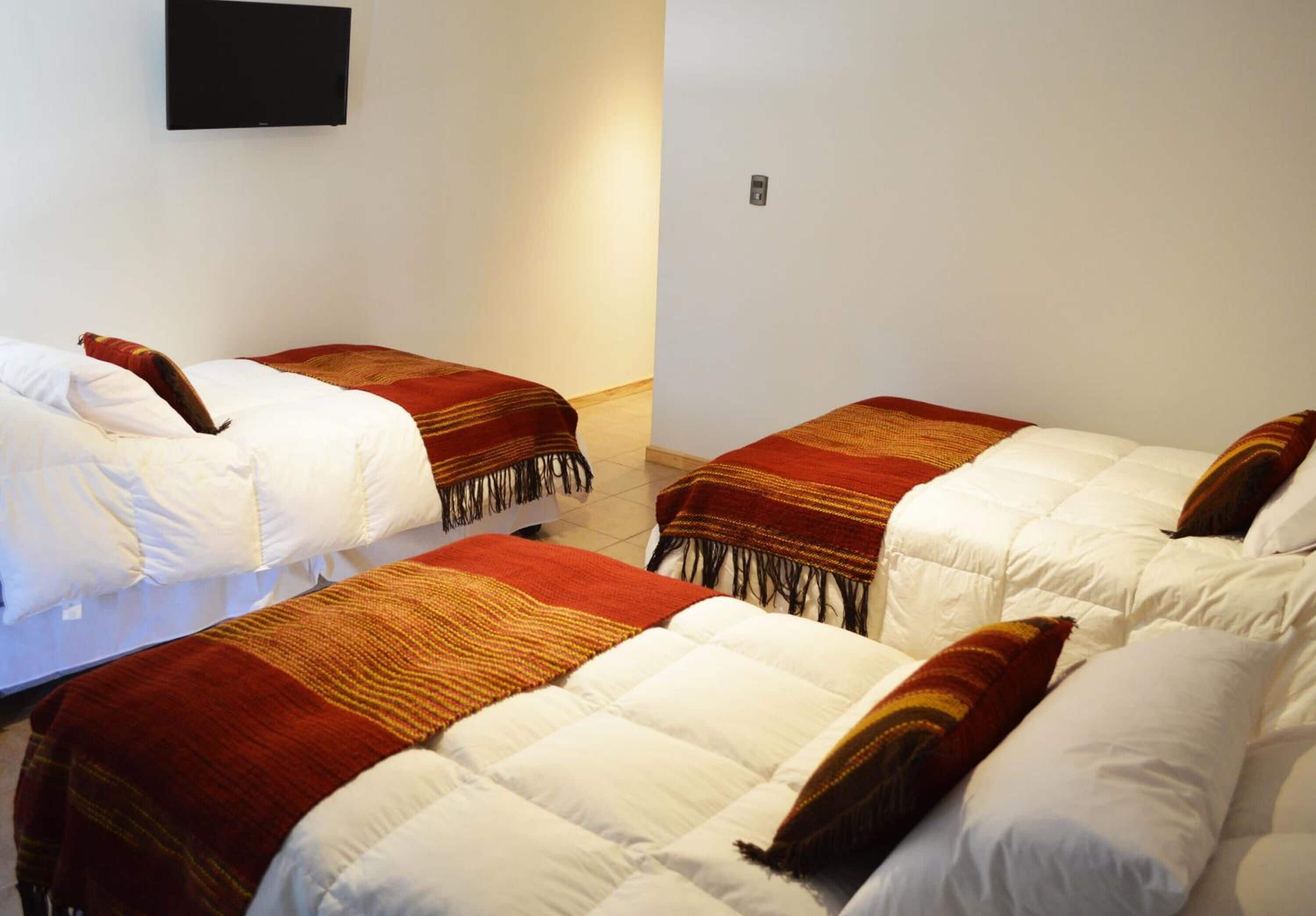 Ein Hotelzimmer mit drei Betten, jeweils mit einer weißen und roten Decke.