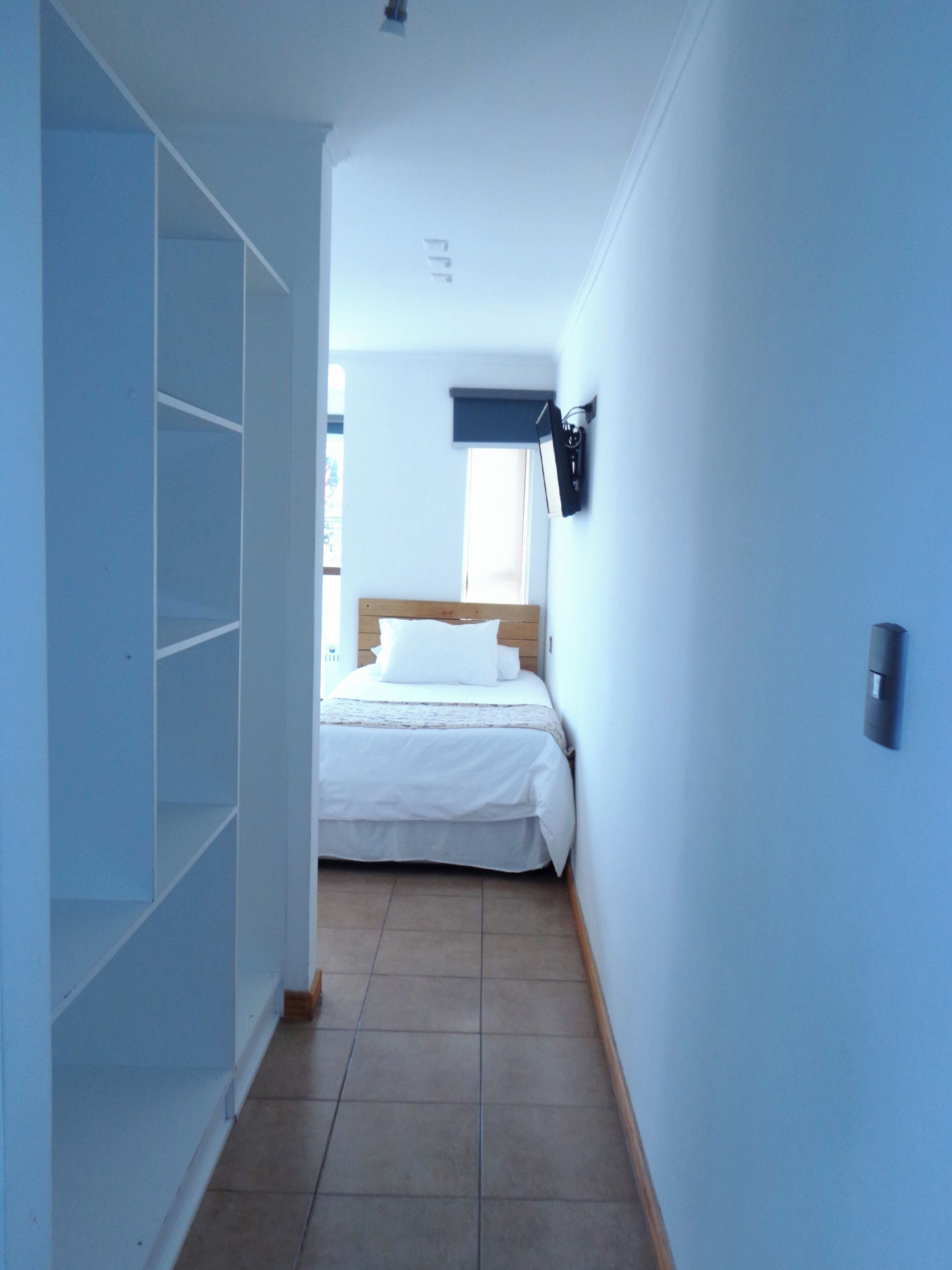 Un dormitorio con cama, armario, ventana y una lámpara fijada a la pared.