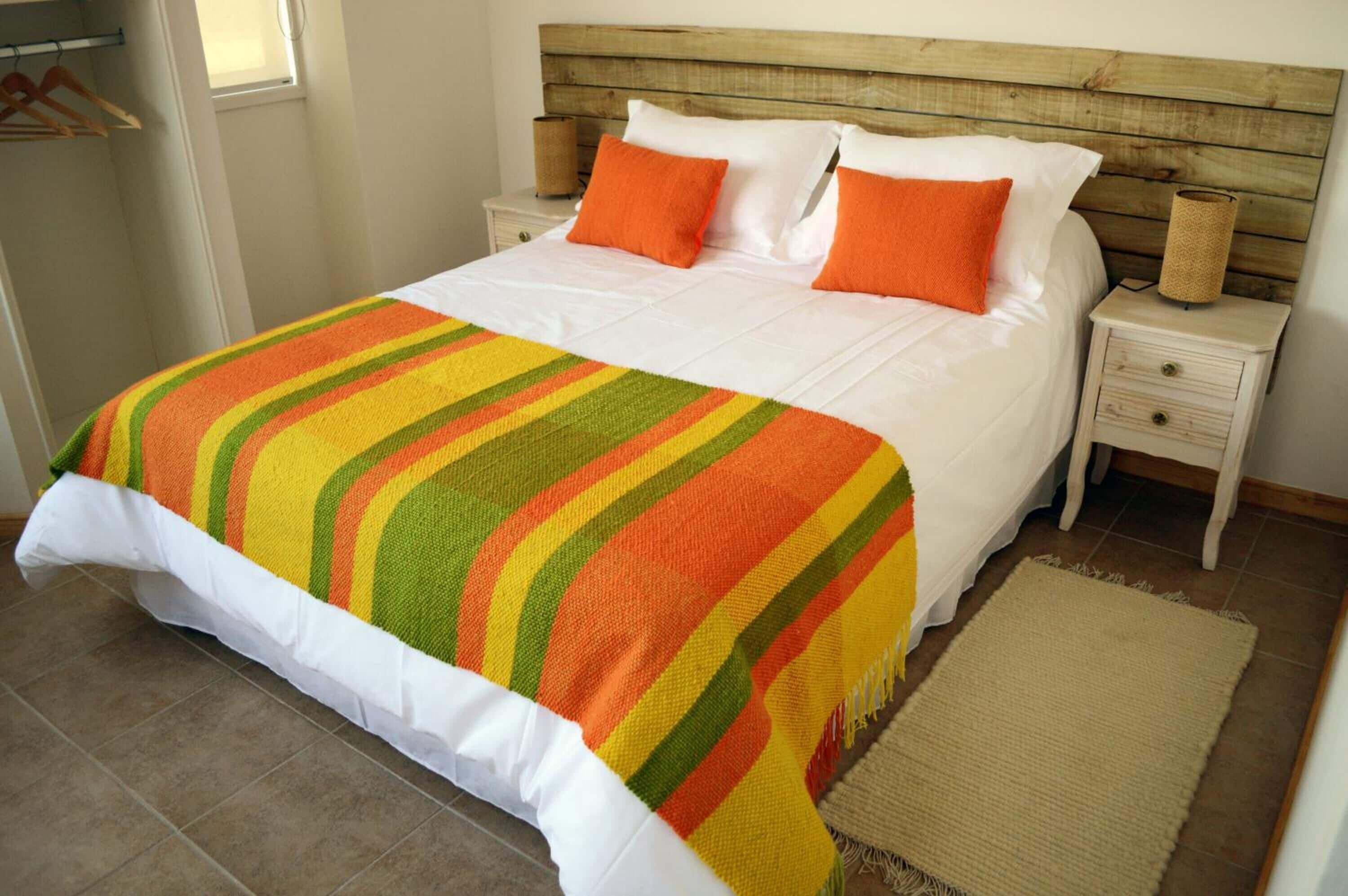 Een bed met een gestreept dekbed, witte kussens en oranje sierkussens.