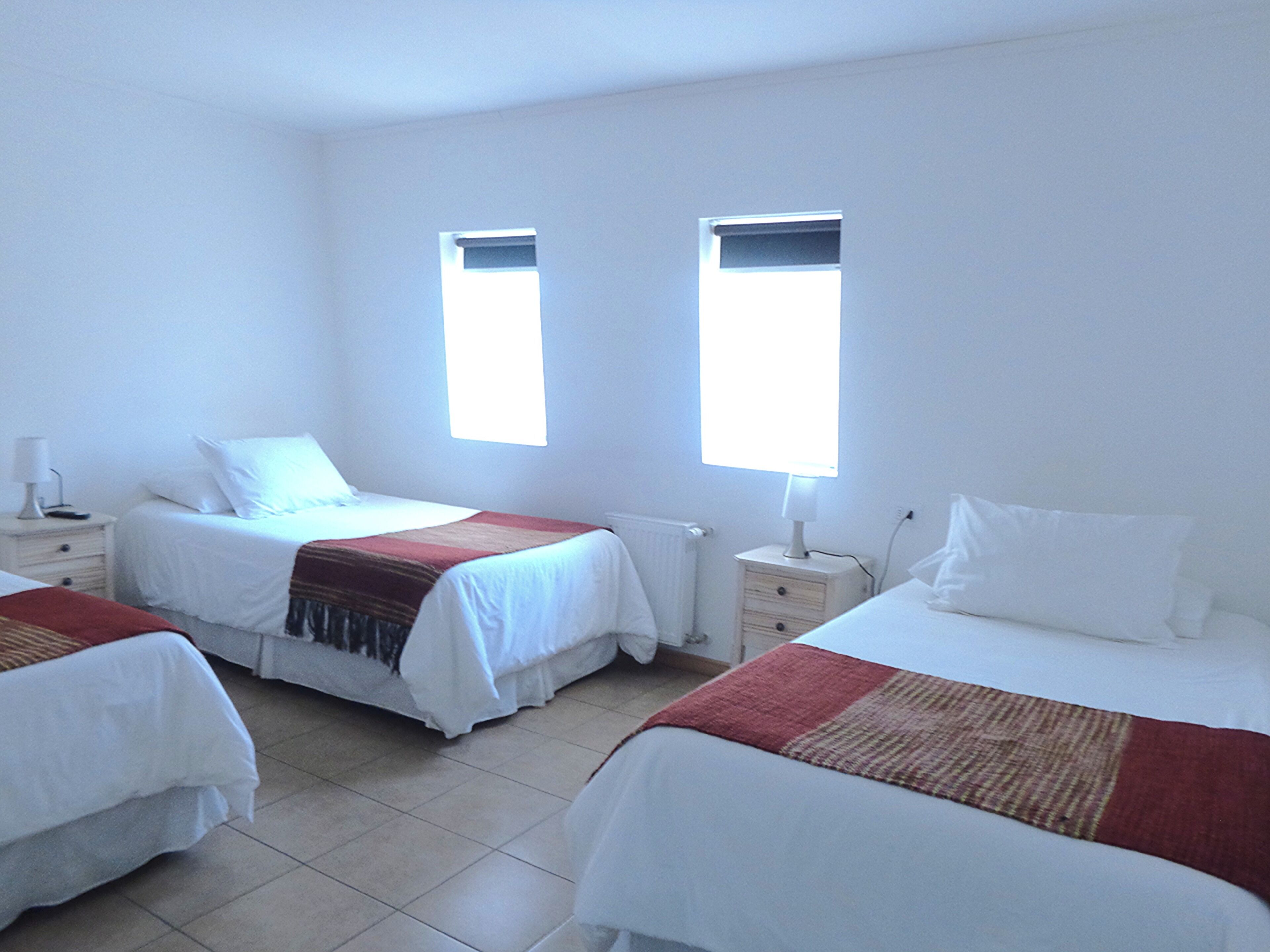 A hotel room with two beds, a window, a nightstand, and a lamp.