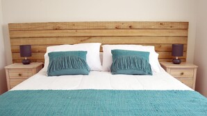 A bed with a wooden headboard, two bedside tables with lamps, and a teal throw blanket. - Apart Hotel Endurance (Punta Arenas)