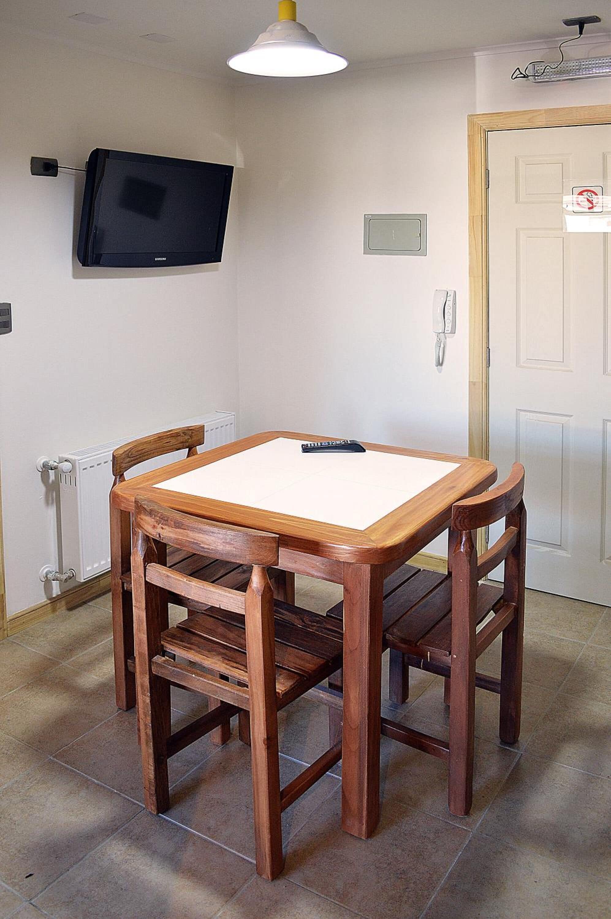A dining area with a wooden table and chairs, a television mounted on the wall, and a door with a sign.