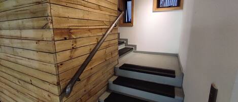 Una escalera de madera con barandal de metal, que conduce a un rellano con un pequeño ventanal.