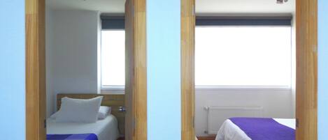 Two adjacent rooms with beds, a window, and a radiator.