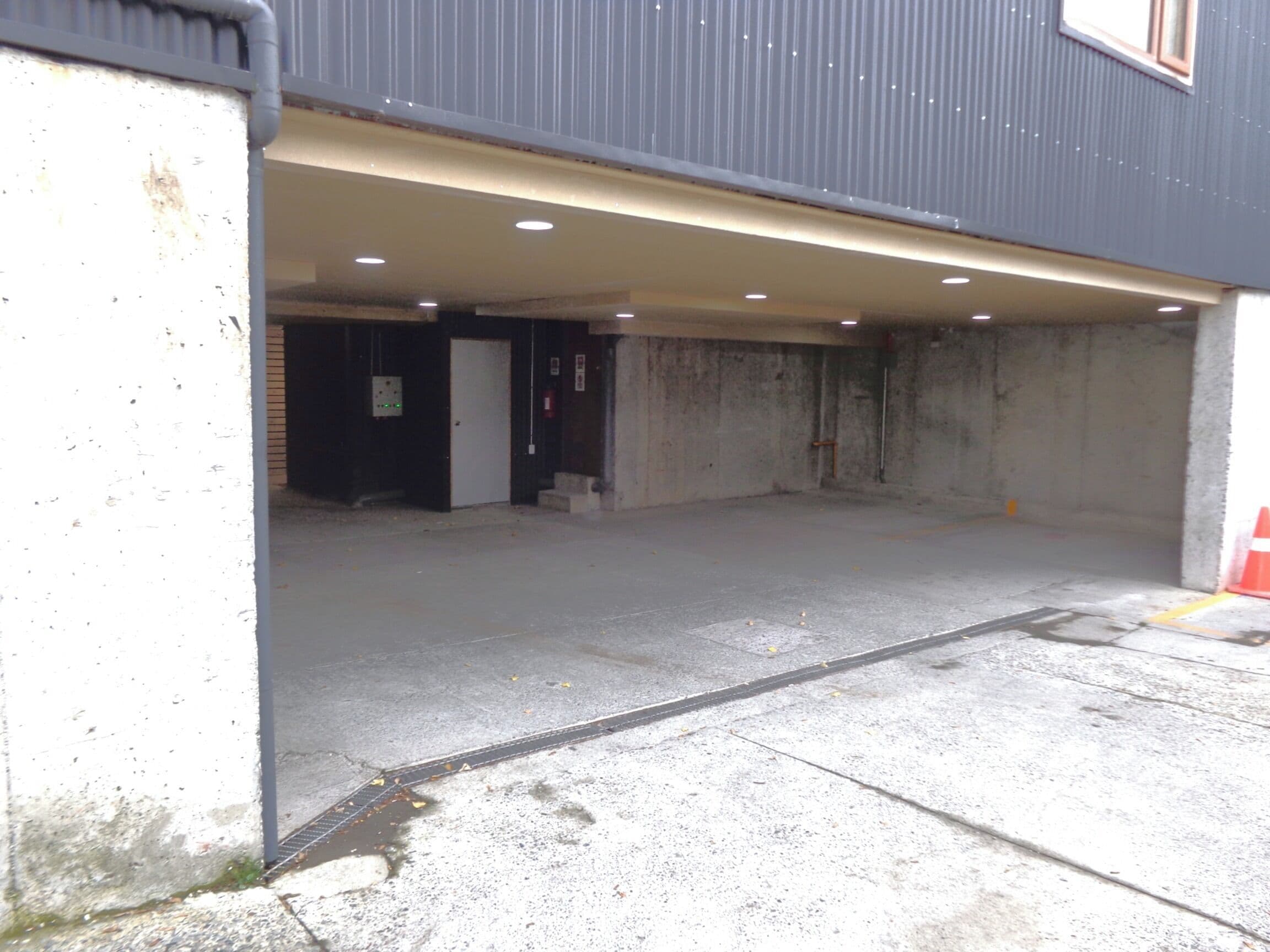 An indoor parking garage with concrete walls, a metal door, and a ceiling with recessed lighting.