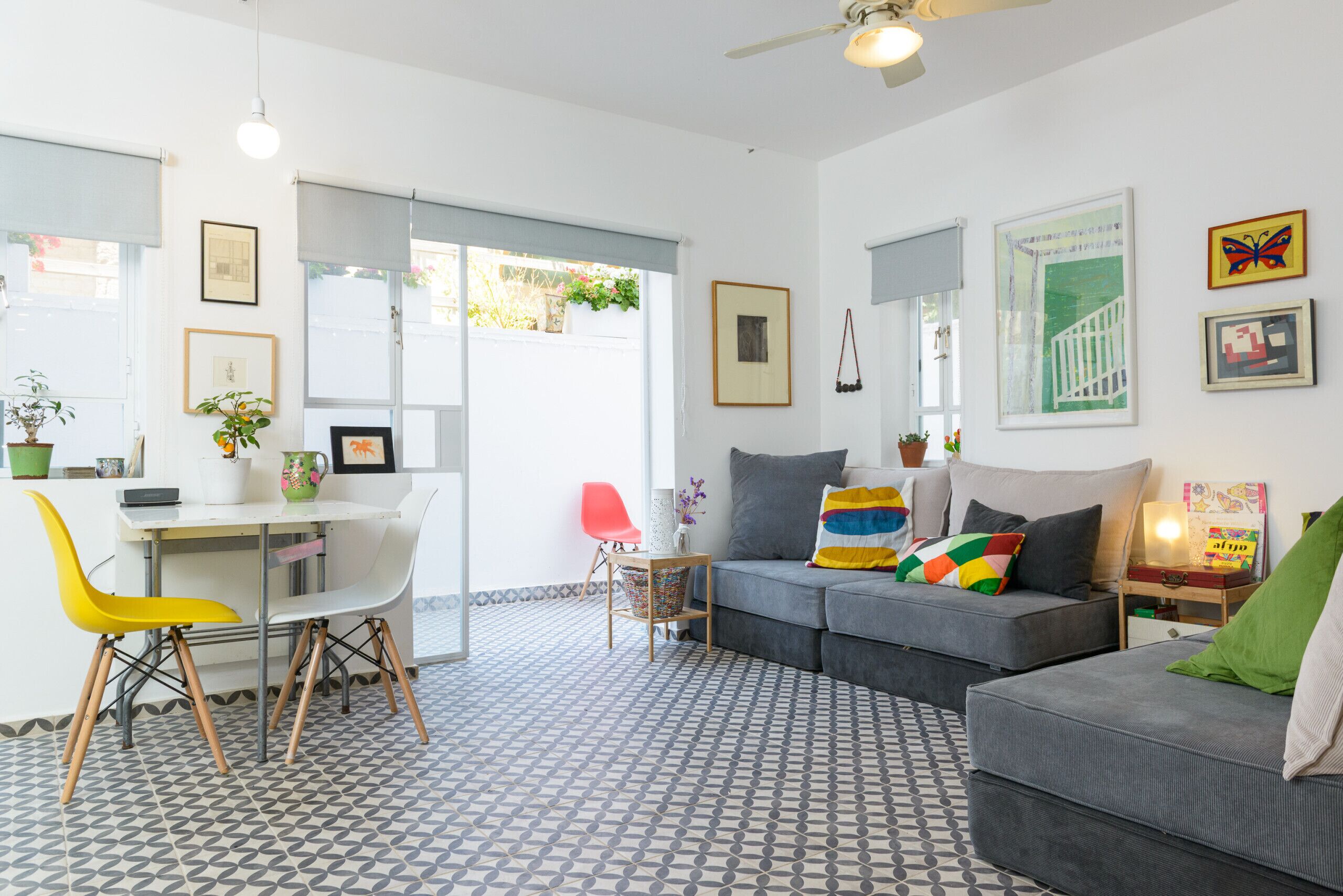 A modern living room with a grey sofa, a dining table with chairs, and a patterned floor.