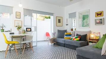 A modern living room with a grey sofa, a dining table with chairs, and a patterned floor.