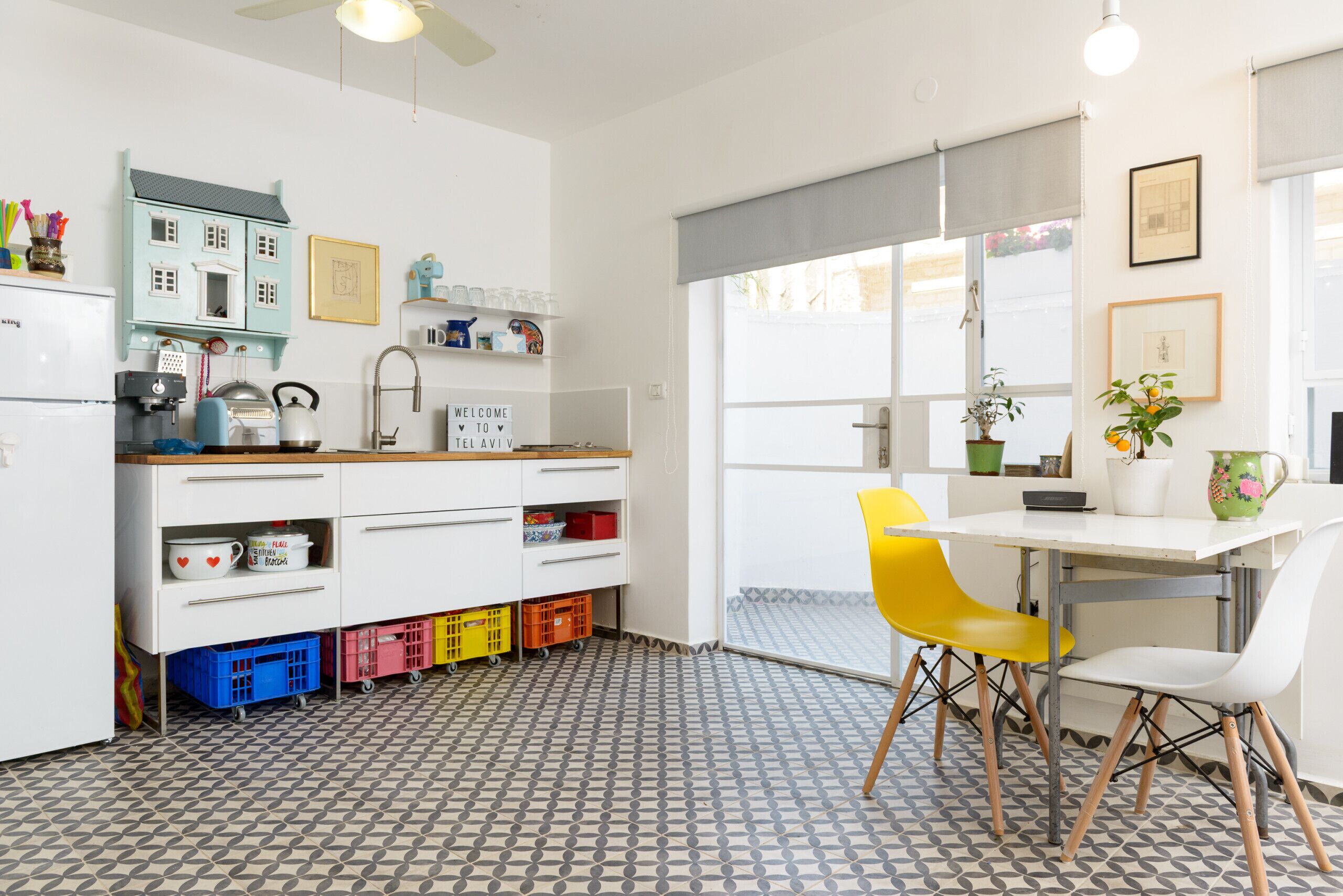 A modern kitchen with a white countertop, a sink, and a dining area with a white table and yellow chairs.