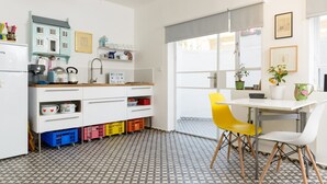 Une cuisine moderne avec un plan de travail blanc, un évier et un coin repas comprenant une table blanche et des chaises jaunes.