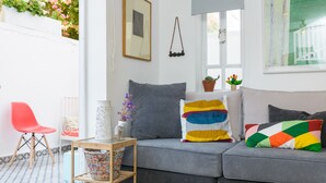 Un salon moderne avec un canapé gris, des coussins colorés, une petite table sur laquelle est posé un vase, et un fauteuil rouge.