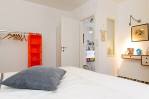 Ein Schlafzimmer mit einem Bett, einem grauen Kopfkissen, einem Kleiderschrank mit orangenen Regalen und einem Flur, der zu einem Badezimmer führt.